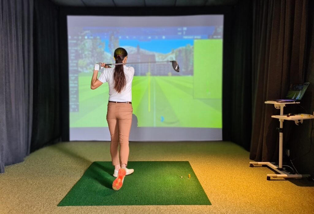 A girl practicing golf shots inside a simulator