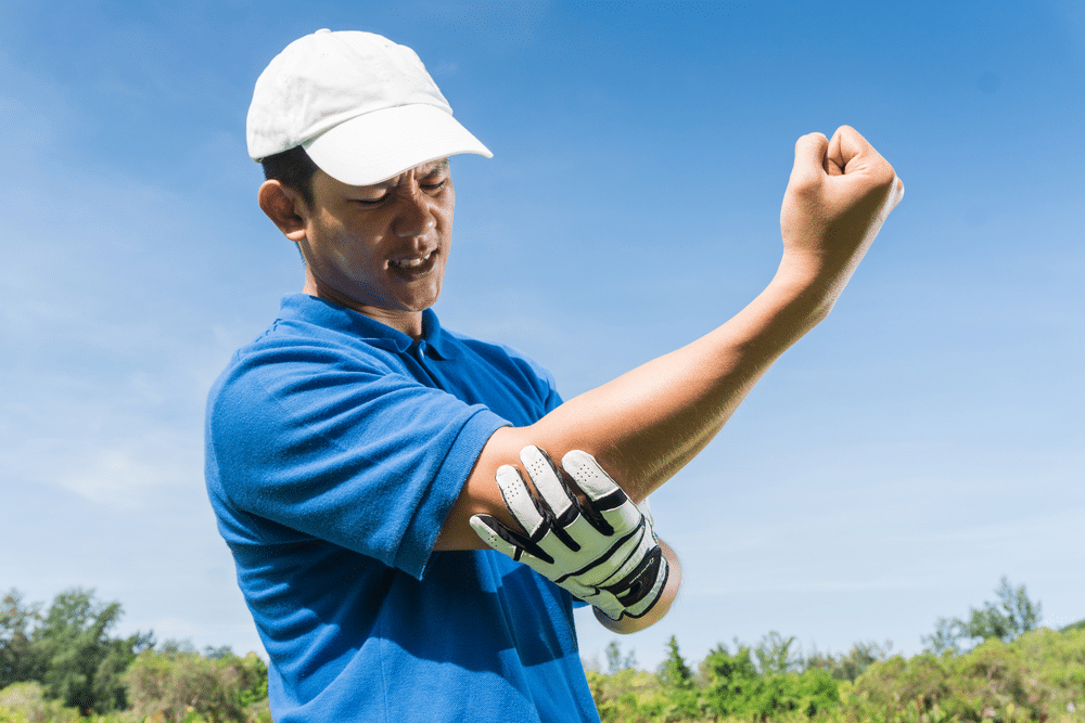 man holding his elbow injured while playing golf