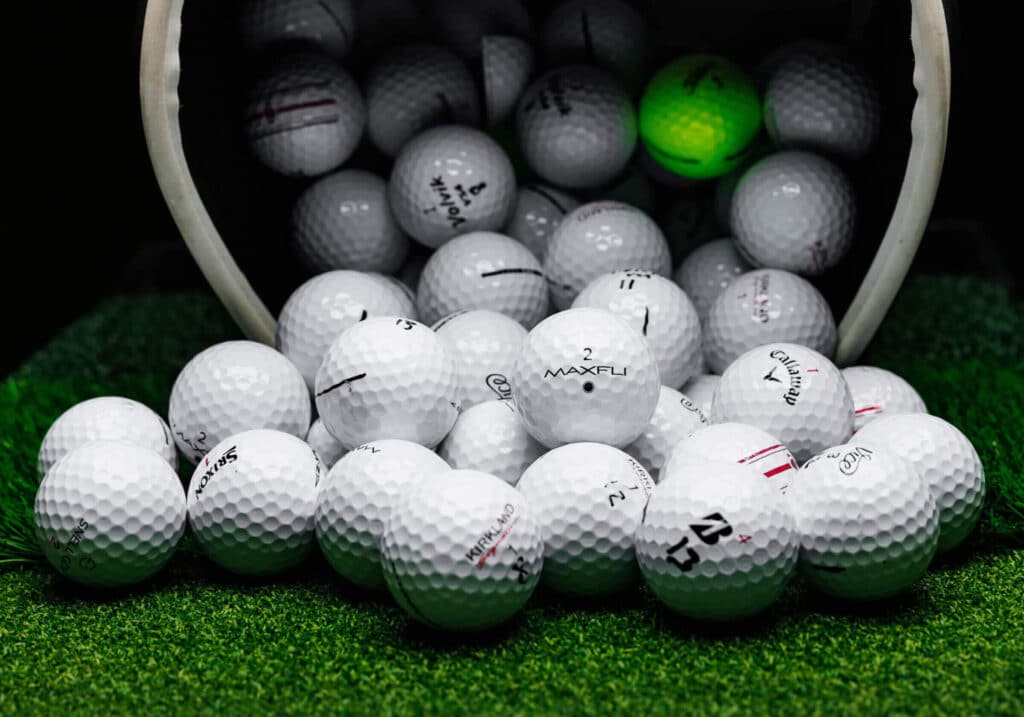 A basket emptying many types of white golf balls on grass