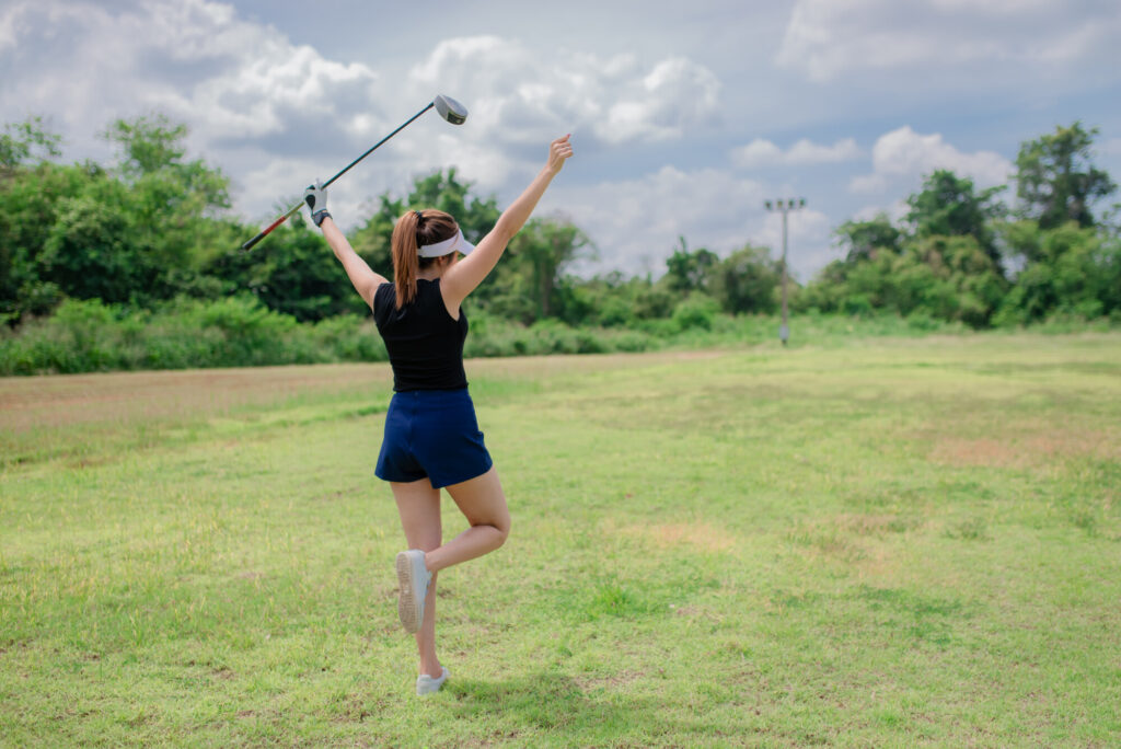 A golfer woman cheering at a golf course lifting one leg