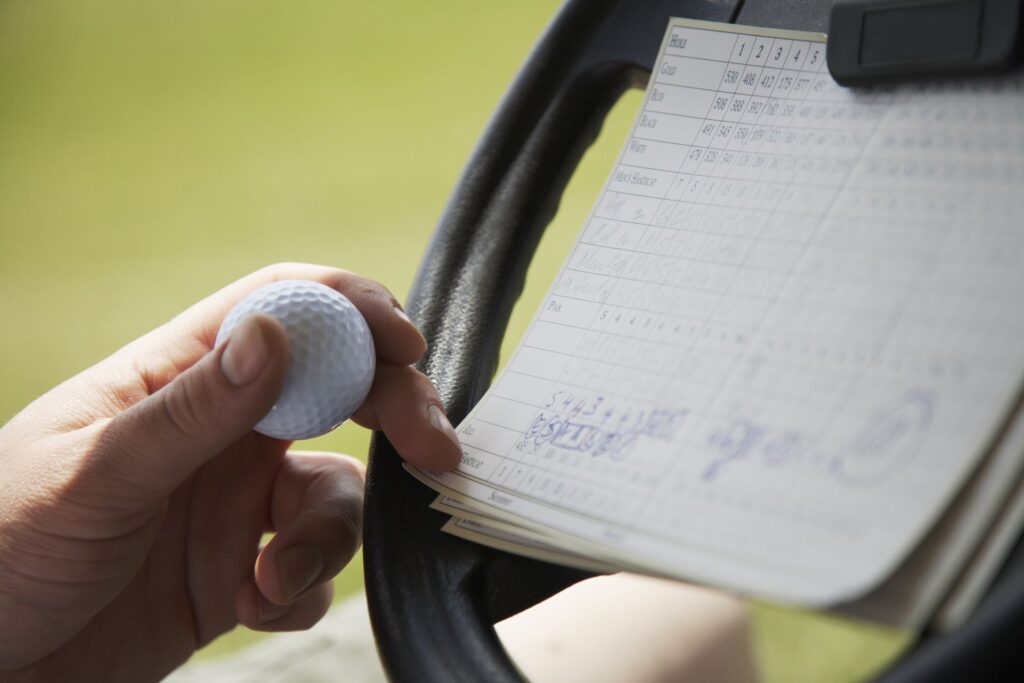 A person holding a golf ball checking a golf scorecard