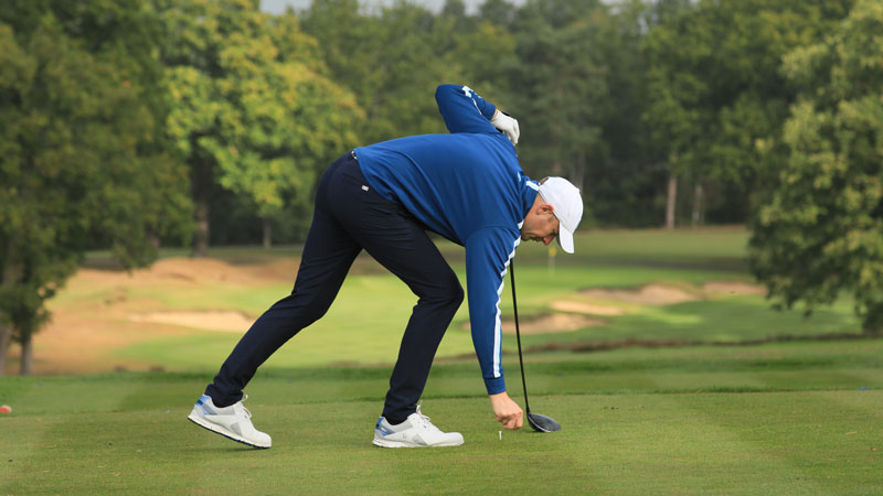 A person placing a golf ball bending over getting ready for a provisional golf shot