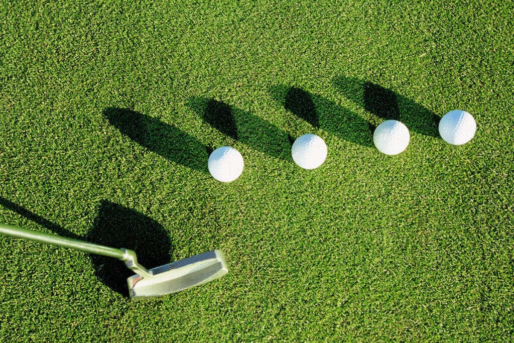 A top view of four golf balls in a grass with a golf club