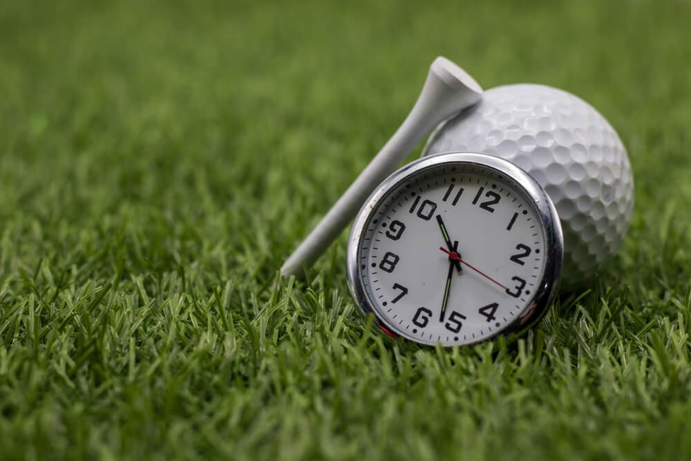 A view of a golf ball a clock and a white tee placed in the grass