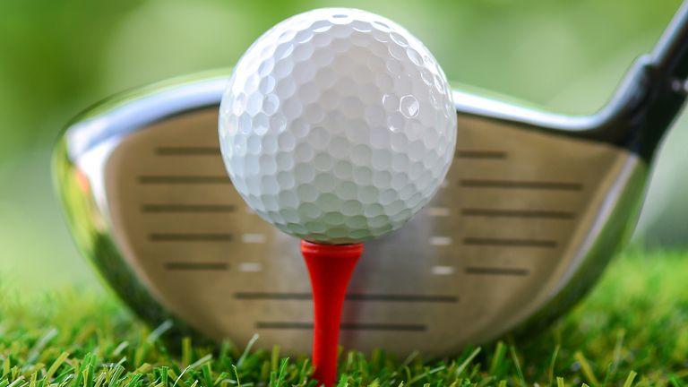 A view of a golf ball on a red tee with a golf club blurred behind it