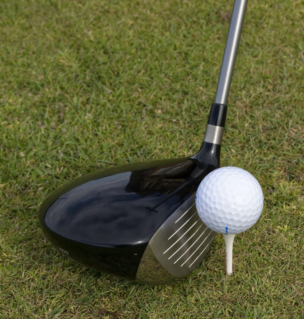 A view of a golf club in grass about to hit the golf ball