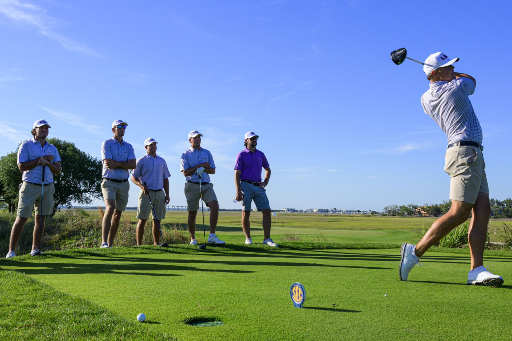 A view of six people at a golf course and one hitting the shot