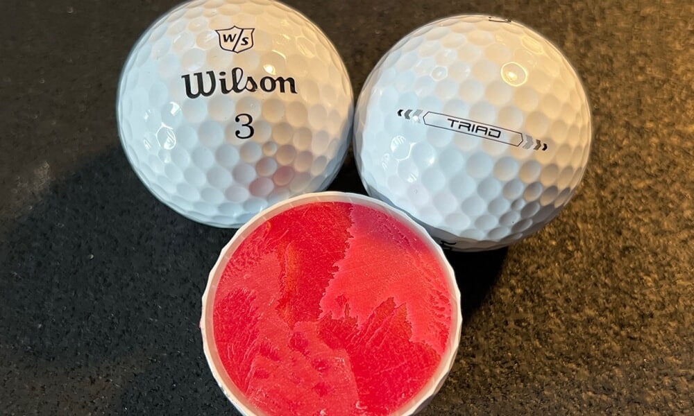 Three golf balls one cut open showing its layers and pink inside