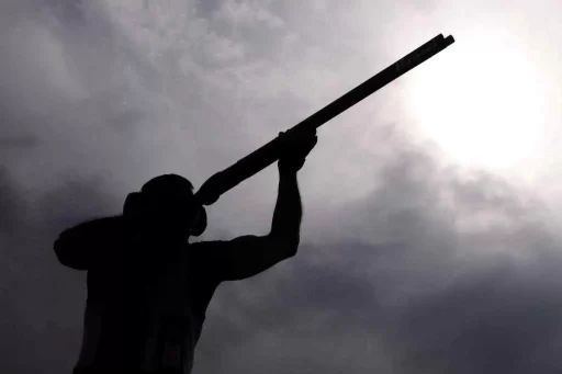 A person in black shadow shooting a shotgun with a view of grey clouds