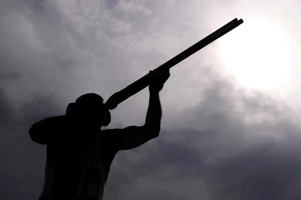 A person in black shadow shooting a shotgun with a view of grey clouds