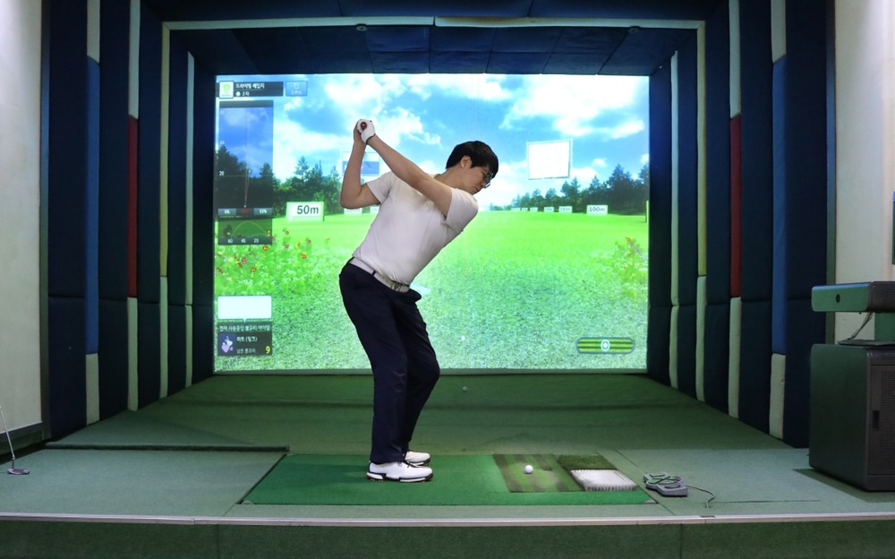 A view of a guy standing in front of a golf simulator about to hit a ball