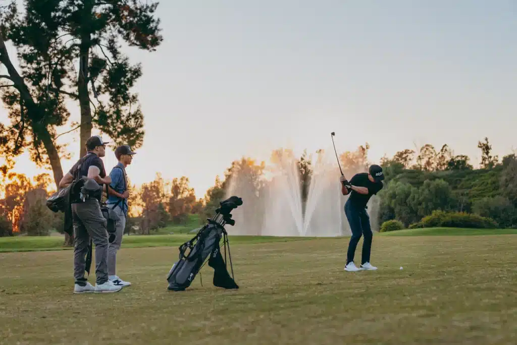 boys in the ground one of then playing golf holding a club and other two watching him