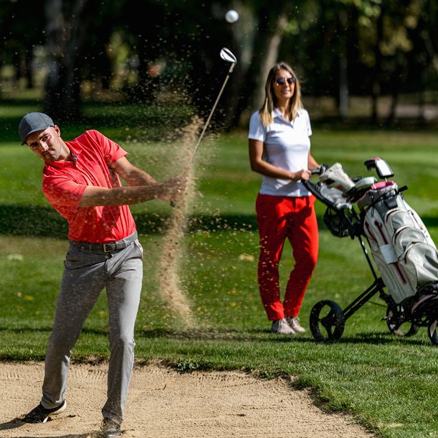 a trainer training female to polay golf female holding a golf club and looking at the ball