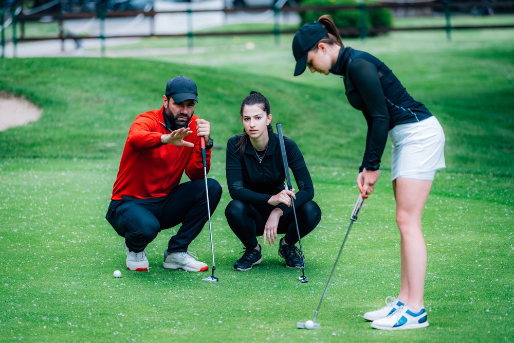 Golf putting lesson, two young female golfers practicing putting with golf instructor