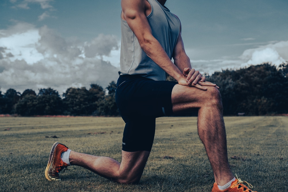 Muscular athlete stretching hamstring and hip flexor in a yoga position on a field