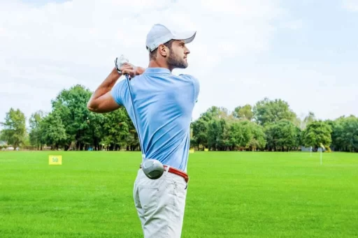 a golfer's side view holding a golf club standing in the ground