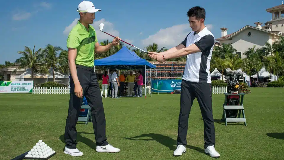 a trainer giving lessons to a boy to play golf in the ground