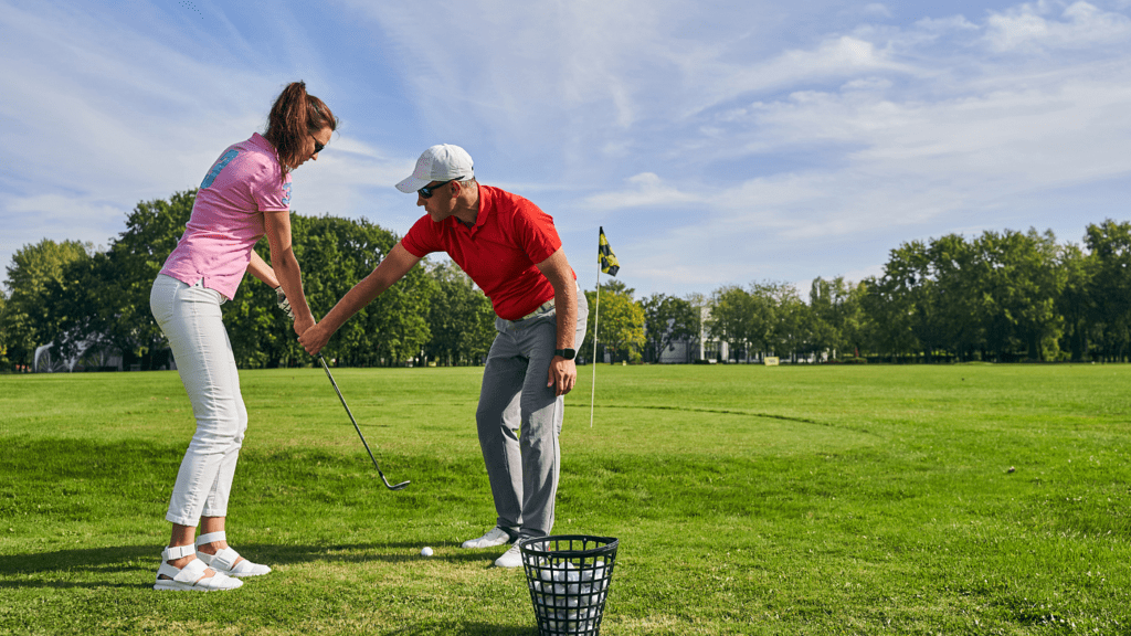 a trainer training female to polay golf female holding a golf club and looking at the ball