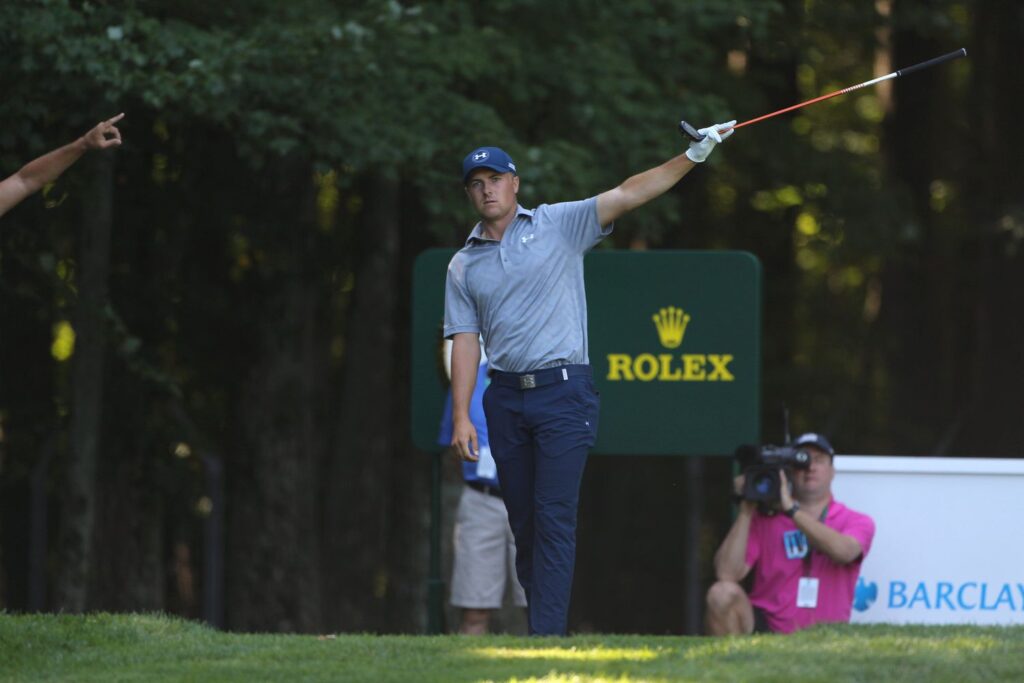 professional golfer holding a club in one hand poiting towards a spot a cameraman behind his back