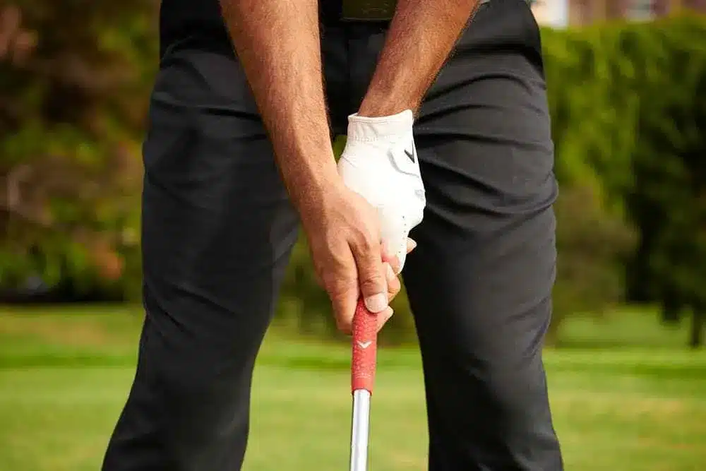 zoomed in view of golfer's hands, one with glove, holding a club in a ground