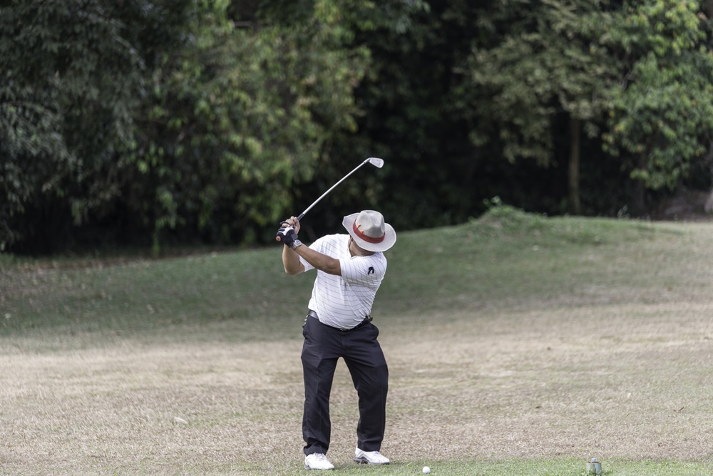 a man in white shirt, holding club face and hitting shot. 